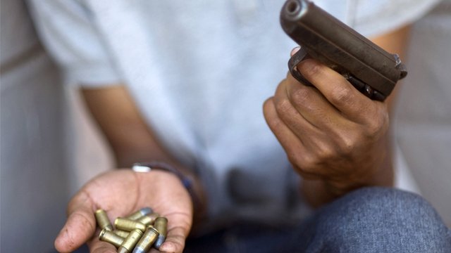 Man sitting down with gun in one hand and bullets in the other